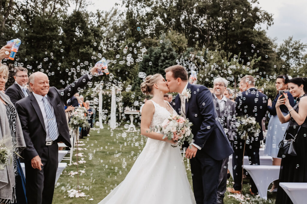 Hochzeitspaar küsst sich nach der freien Trauung. Gäste machen Seifenblasen.